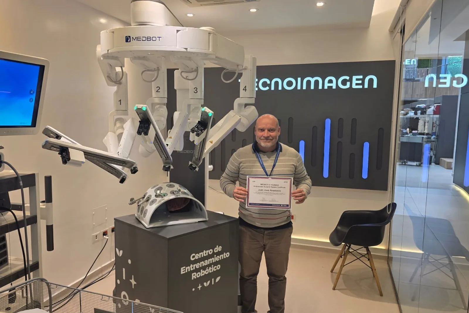 El Dr. Anastasio con su certificado de entrenamiento, junto a un sistema quirúrgico robótico en el centro de formación.